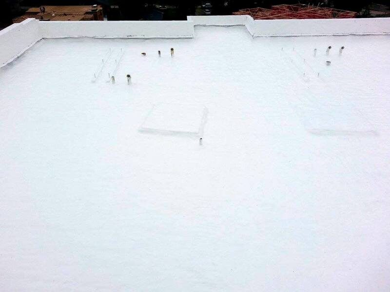 Commercial flat roof with a freshly applied white roof coating, parapet walls and penetrations