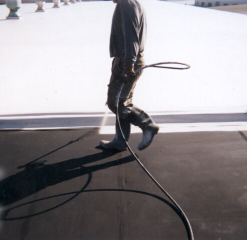 Roofer applying an elastomeric top coat across a commercial flat roof