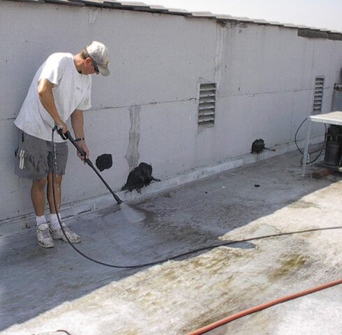 Roofer power washing an existing commercial flat roof to prepare it for a roof coating
