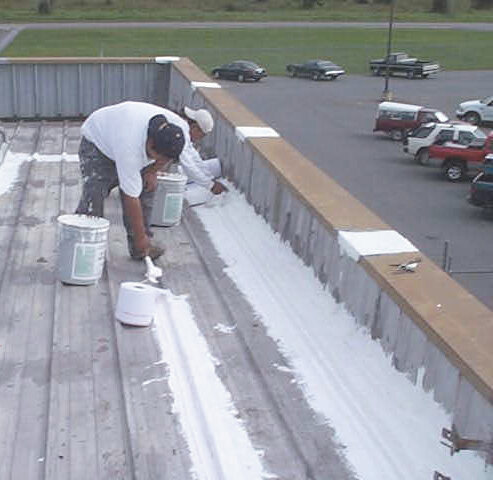 Roofers preparing the seams of a commercial metal roof before applying a roof coating